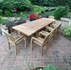 Recycled teakwood outdoor table and stacking chairs dining set on a brick patio with garden in the background